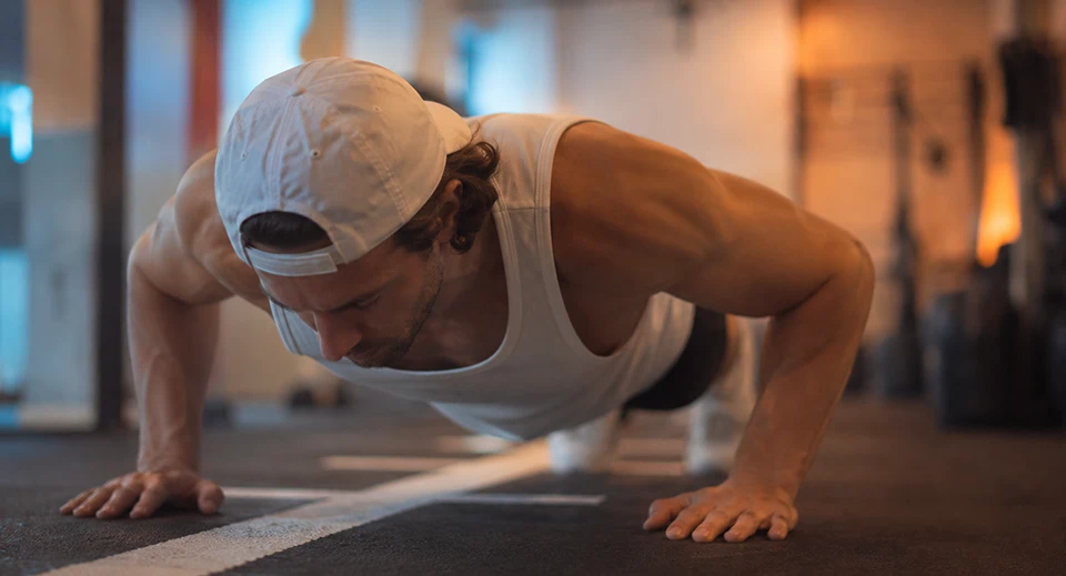 Athlete in a white cap doing push-ups on a gym floor during a hybrid training session